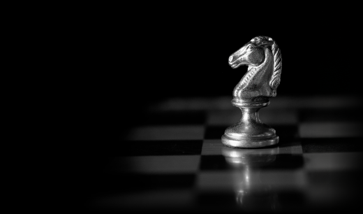 Silver knight chess piece on a dark, reflective chessboard with dramatic lighting.