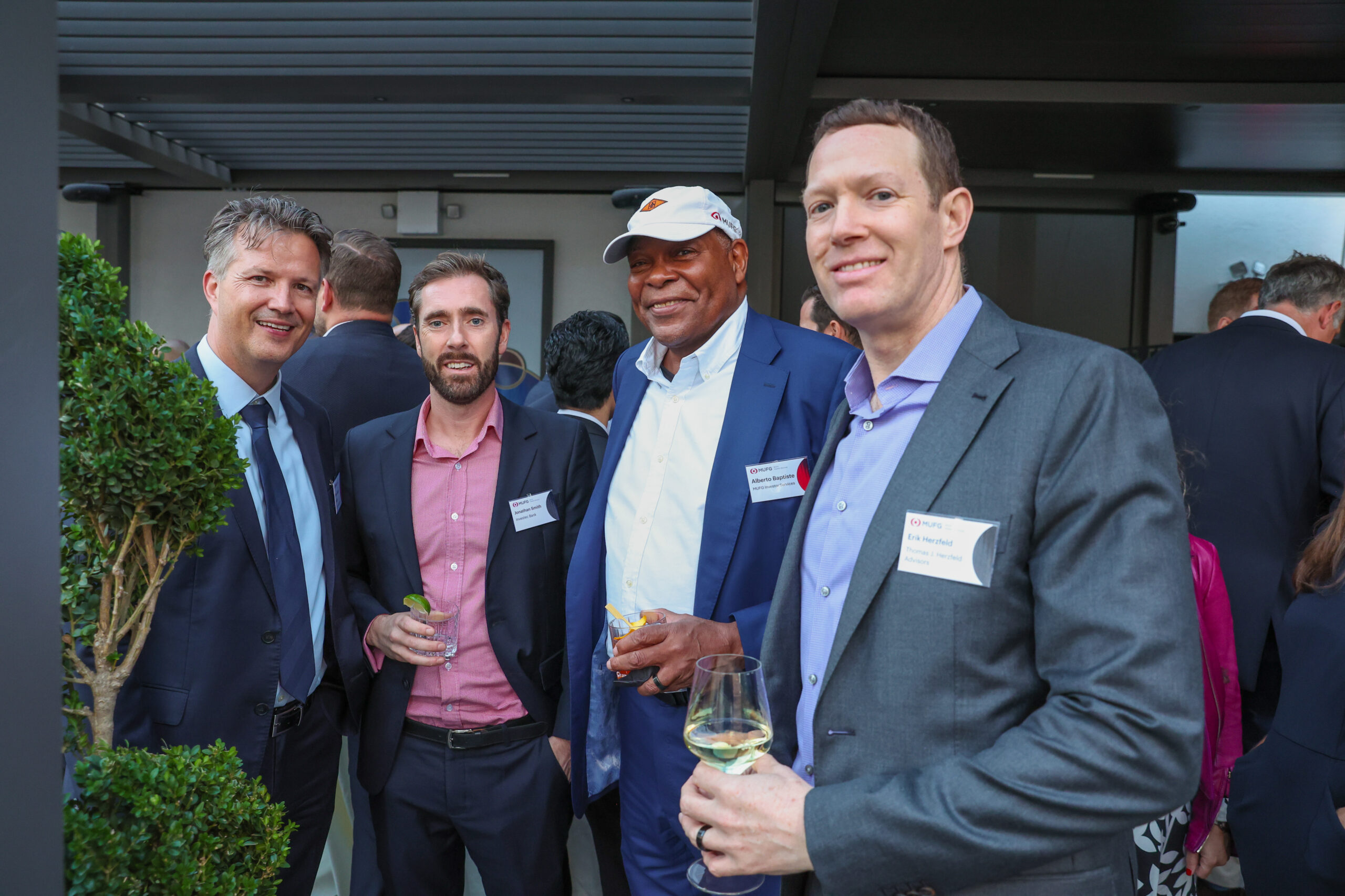 Group of suited professionals at a social event, wearing name badges and holding drinks.