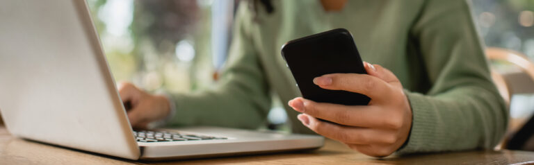 partial view of african american woman holding phone near laptop