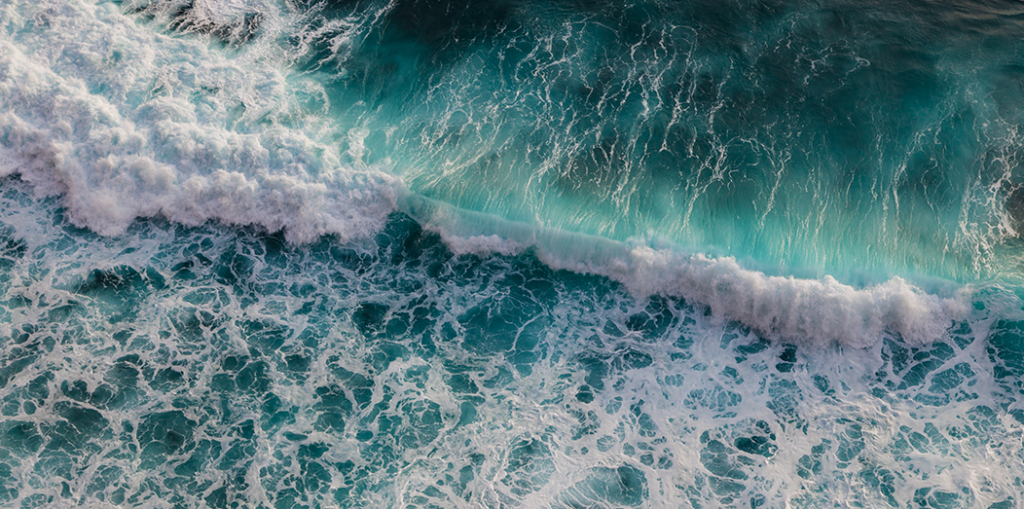seashore with rolling waves crashing on rock coast with spray and foam, view from a height of 100 meters, uluwatu, bali, indonesia